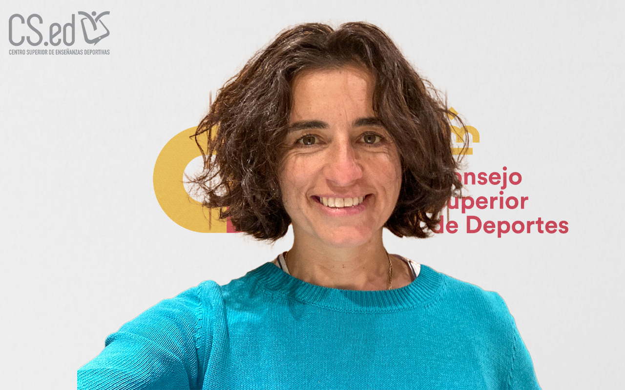 La imagen muestra a una mujer con cabello castaño corto y rizado sonriendo a la cámara. Lleva una sudadera azul turquesa y está de pie frente a una pared blanca con el logotipo de "Consejo Superior de Enseñanzas Deportivas" en la parte superior.